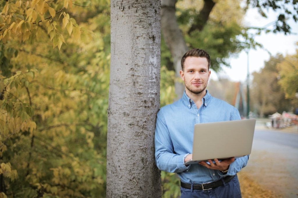 a man standing outside with his laptop thinking if he should start an online vs offline business